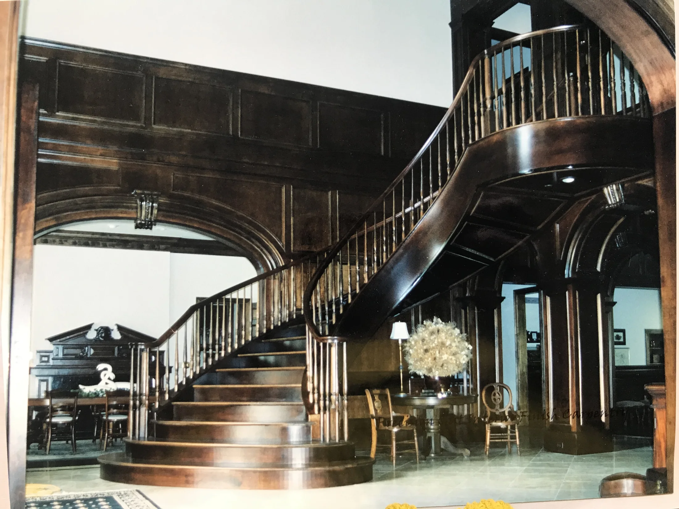 Sweeping curved dark wood staircase with paneled walls and custom railing
