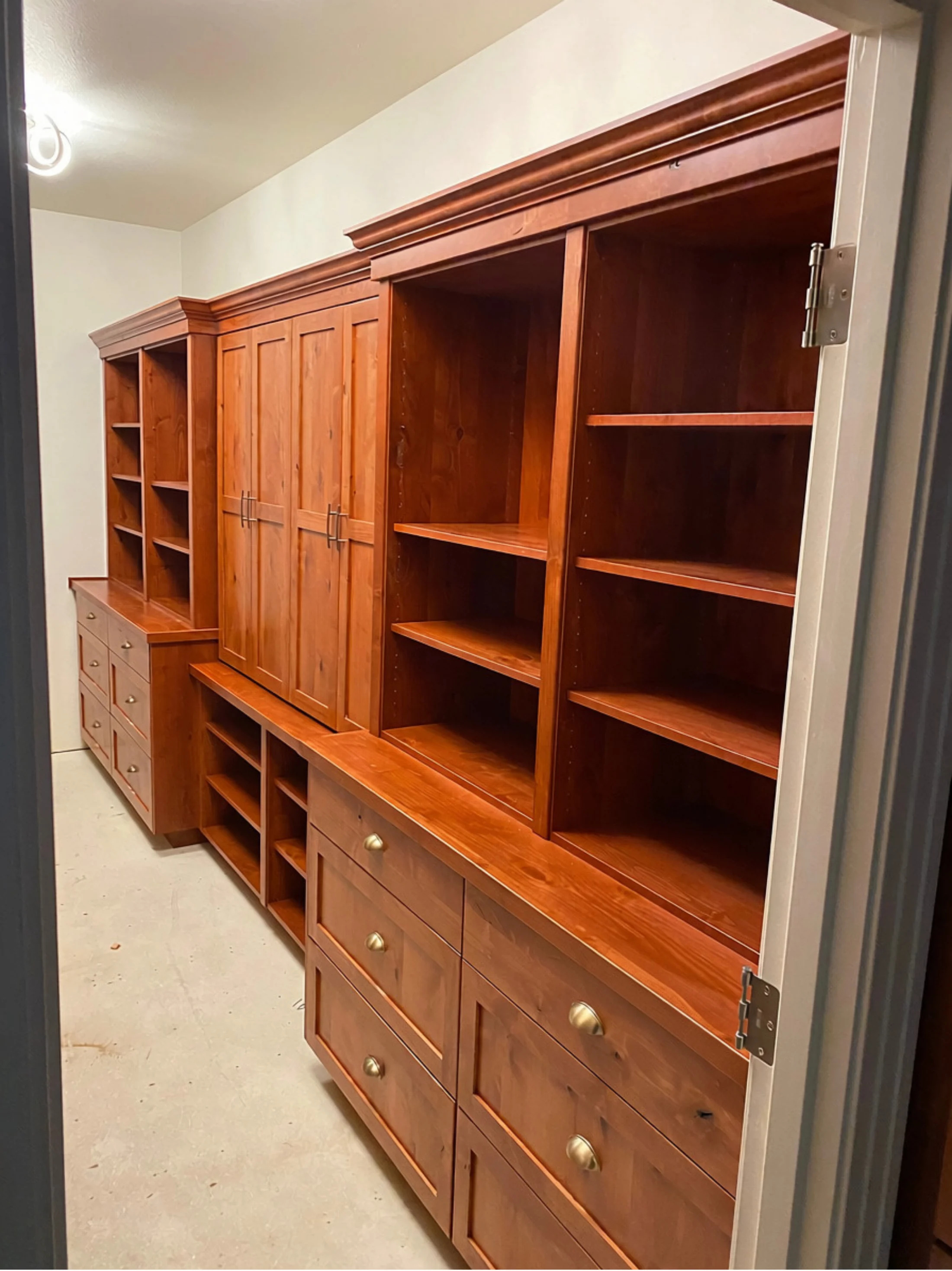 Completed wall-to-wall cherry built-in with drawers, shelving, and detailed crown